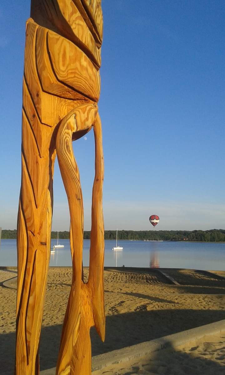 La sculpture 333 sur une plage au bord d'un lac, une montgolfière dans le ciel.