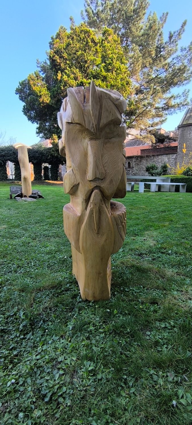 Visage sculpté dans un tronc clair, sur la pelouse d'un jardin.
